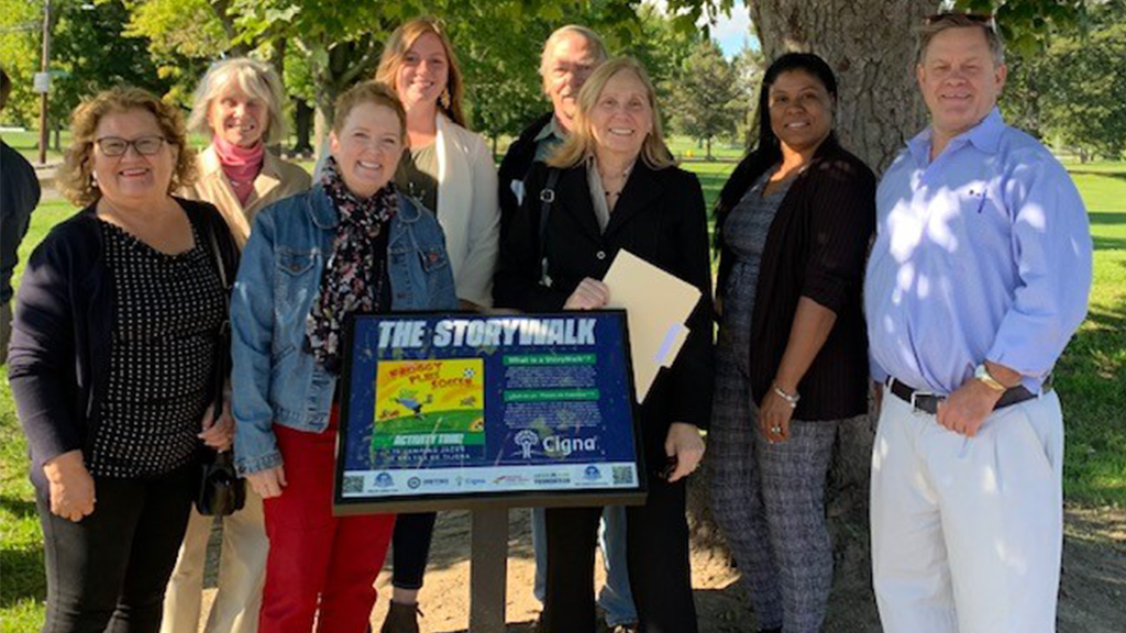 a group of people smiling and holding a poster of Storywalk in a park