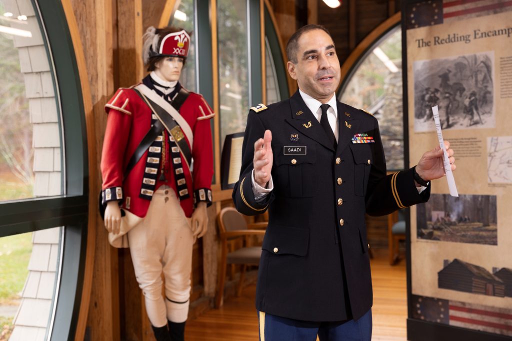 veteran affairs commissioner Thomas Saadi in military uniform standing in front of a statue of a revolutionary war soldier
