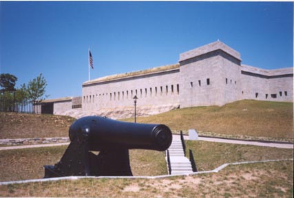 a black cannon sitting in front of Fort Trumball, a large white building