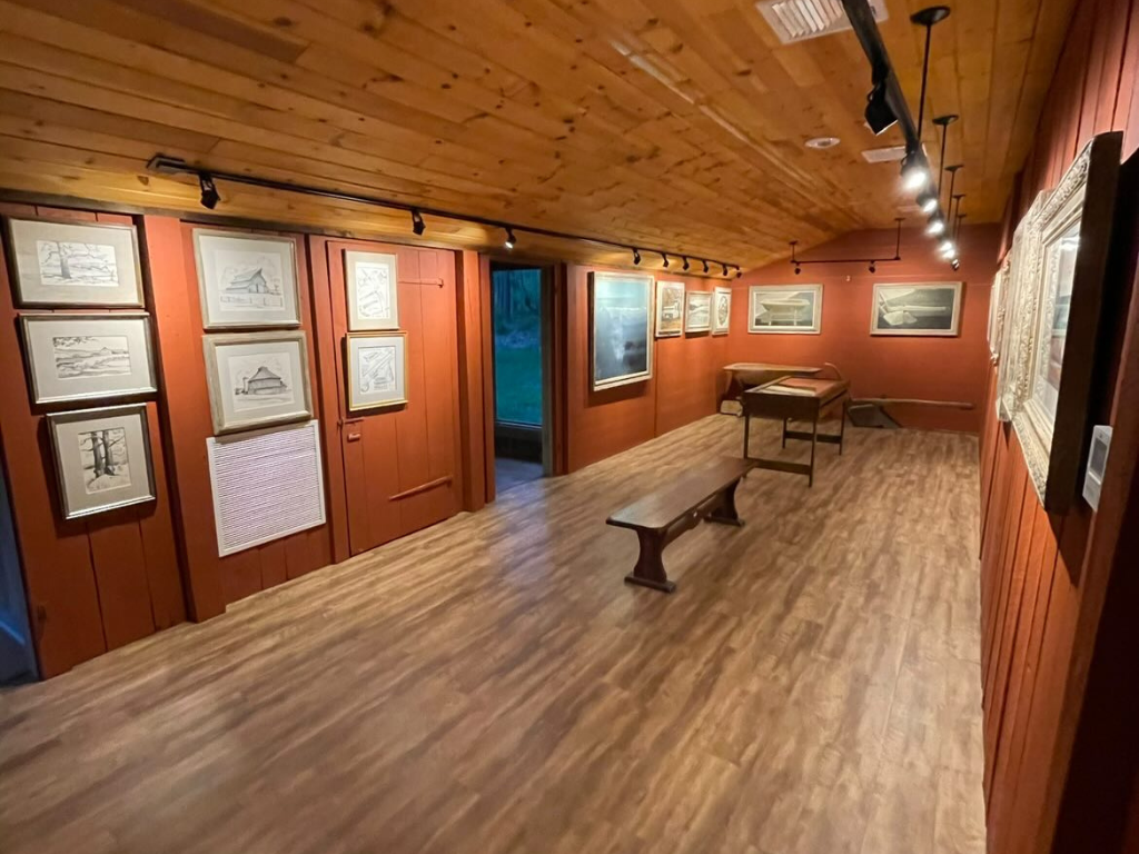 a room inside the museum with framed illustrations hanging o the walls, the floor and ceiling are wood and the walls are painted a dark orange