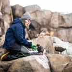 a person kneeling on rocks and feeding puffins