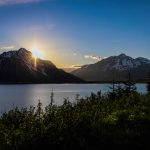 a photo of the sun rising over a mountain with water in front it