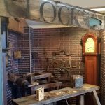 a wooden table in front of a brick wall and a grandfather clock