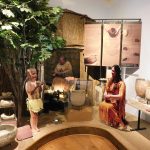 Museum exhibit depicting Indigenous daily life, with mannequins of adults and a child in traditional clothing, pottery displays, and interpretive panels.