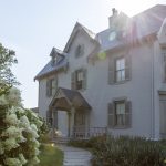 Historic white Victorian-style house with landscaped garden and sunlight streaming across the roof