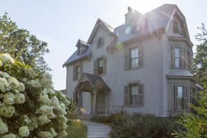 Historic white Victorian-style house with landscaped garden and sunlight streaming across the roof