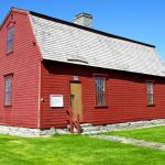 Trumbull War Office “Historic small red wooden Trumbull War Office with a steep shingled roof, stone chimney, wooden door, and multi-pane windows, surrounded by green lawn and stone walls.”