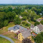 Aerial view of the Webb Deane Stevens Museum campus, showing several historic colonial-era houses surrounded by expansive lawns, mature trees, gardens, and pathways, with the Hartford skyline visible in the distance.”